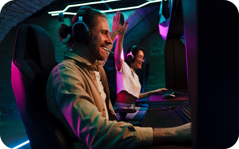Two gamers intensely focused on a 4K monitor in a dimly lit room, enjoying an immersive video game experience.
