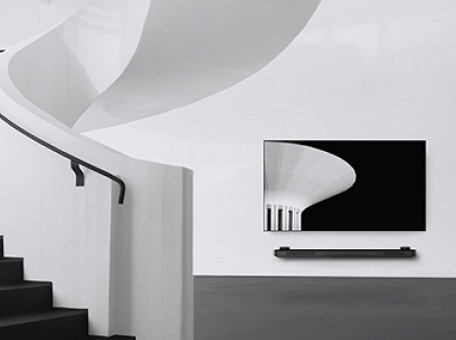 a black and white image of lg signature oled tv which is hung on the wall and to the left there is a spiral staircase