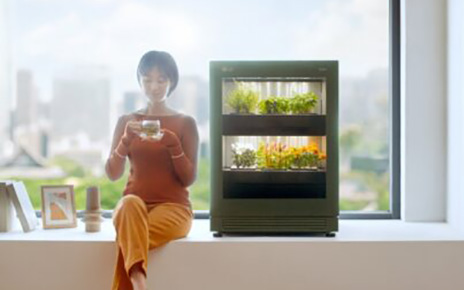 A woman sitting on a large windowsill that looks out on the city as she enjoys a cup of tea next to LG tiiun.