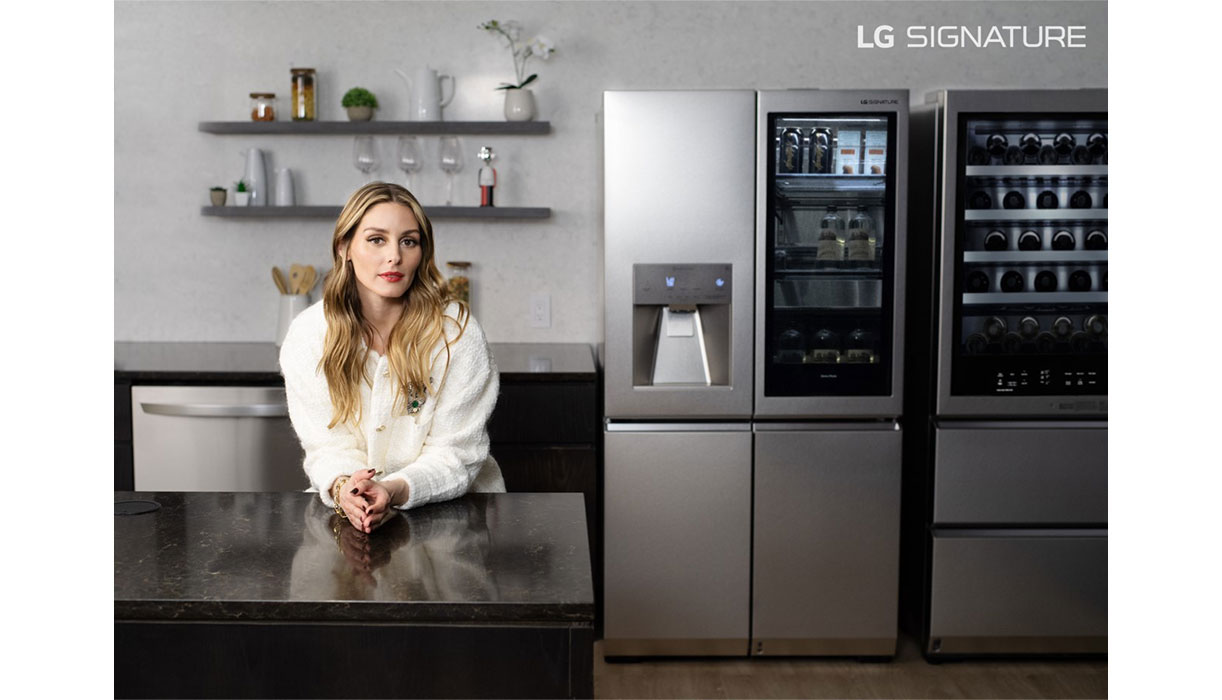 Olivia Palermo is leaning on the LG SIGNATURE Washer/Dryer Combo, positioned between a hanger and laundry trolley