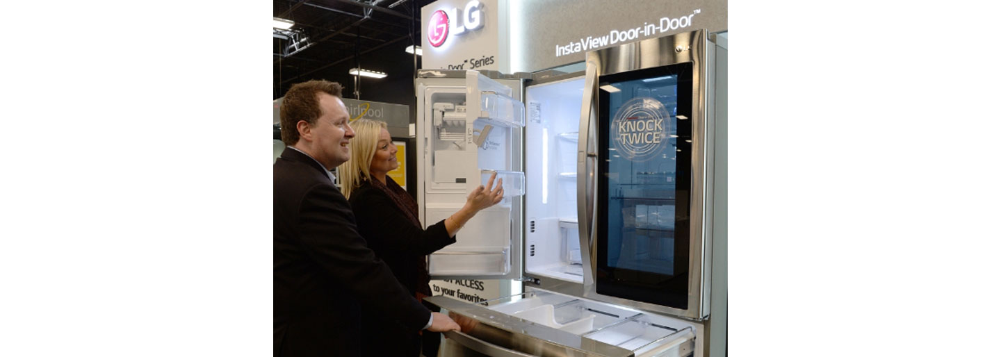 A man and woman take a closer look at the technology found inside the LG InstaView Door-in-Door refrigerator by opening its fridge door compartment