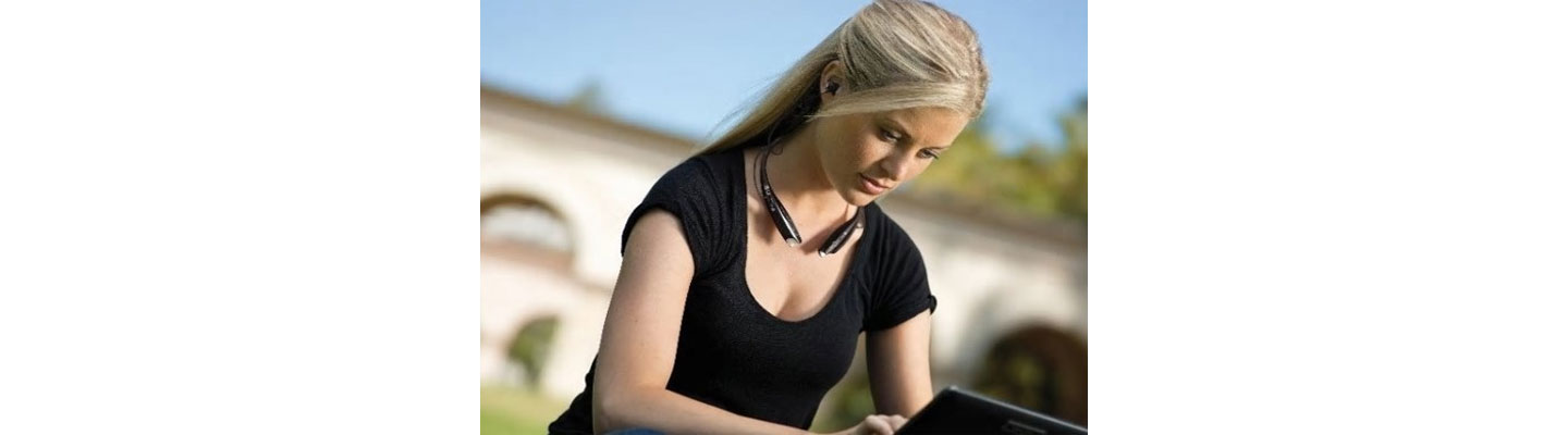 A woman wears the world's first LG Tone Ultra HBS-800 behind-the-neck Bluetooth stereo headset while working on her laptop outdoors.