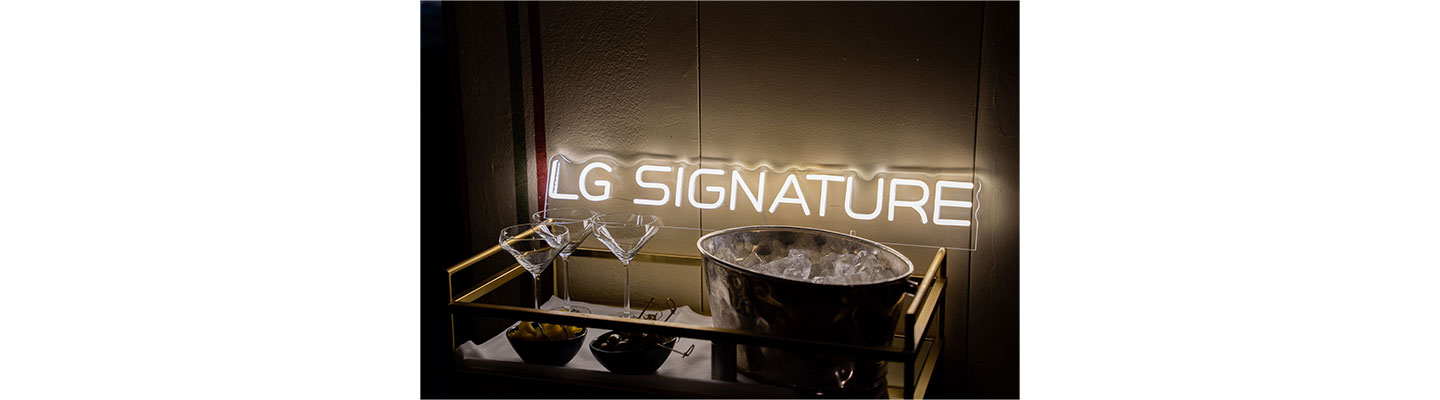 A photo of a LG SIGNATURE sign placed behind the champagne glasses, a cup of olives and a bucket of ice