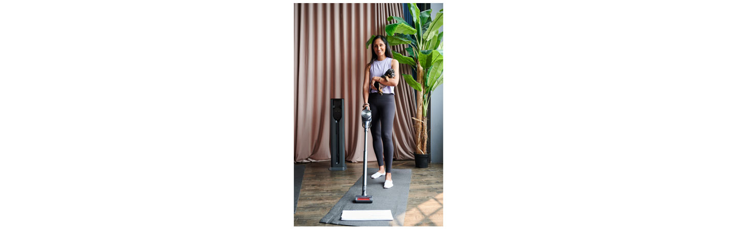 A woman using LG CordZero vacuum to clean up her space after working out while holding a puppy in her arms