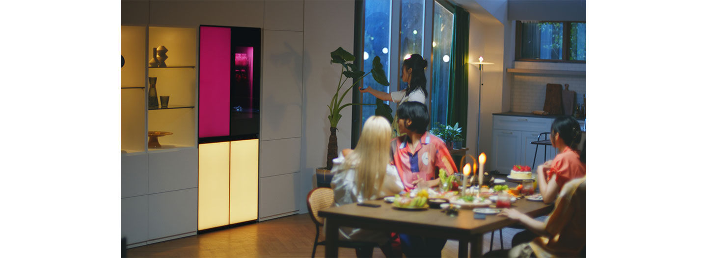 A woman is remotely playing music via a built-in Bluetooth speaker of the LG MoodUPTM refrigerator at the house party