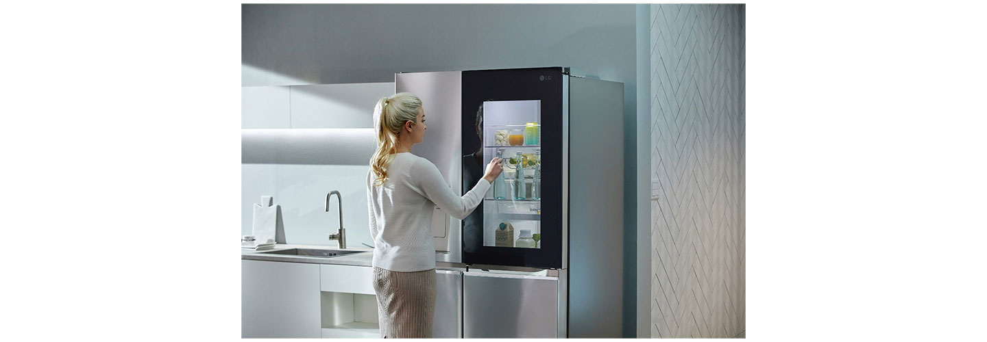 A woman knocking on her LG Door-in-Door refrigerator’s window to look inside without opening the door