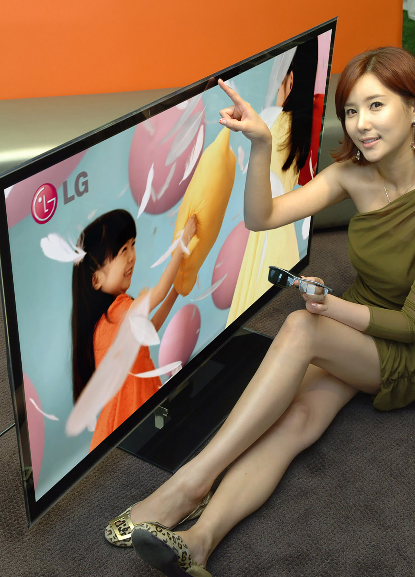 A female model wearing 3D glasses tries to touch the screen of LG's LW980S 3D LCD TV while the TV displays little girls playing a pillow fight.