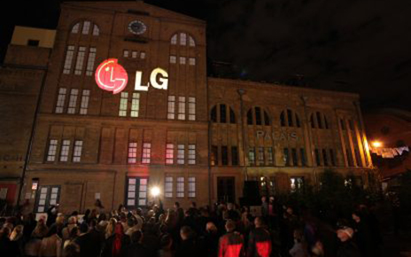 A large audience observes a gigantic 3D LG logo projected onto the front of a building in Kulturbrauerei, Berlin.