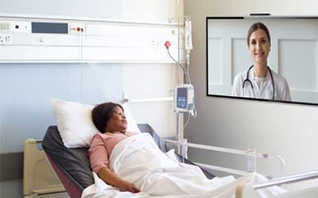 A patient who is resting in a bed is having a video chat with her doctor with the help of LG healthcare TV installed on the wall.