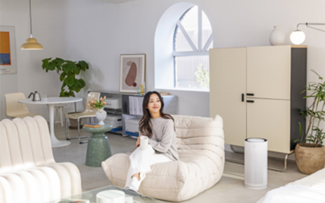 A photo of the LG PuriCare AeroHit set up in a living room besides set up in a living room beside a woman sitting on a sofa