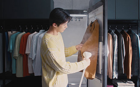 A photo of a man using a handheld high-pressure steamer attached to the LG Styler on a shirt in a dressing room