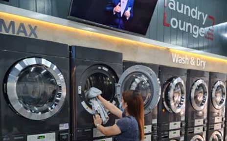 A woman is putting laundry into dryer at Laundry Lounge.