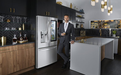 A man in suit standing in front of LG InstaView Door-in-Door™ refrigerator in a kitchen, holding a glass of beverage with Craft Ice™