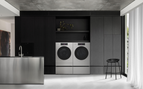 An SKS WashCombo™ and SKS dryer are placed side by side in a modern laundry area with dark cabinetry, open shelving and a large window.