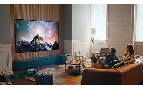 A family together in their living room enjoying spectacular natural landscape images on their wall-mounted 2022 LG OLED TV.