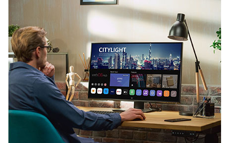 A man sitting at a desk explores the home UI of the new webOS Hub 2.0S on an LG smart monitor