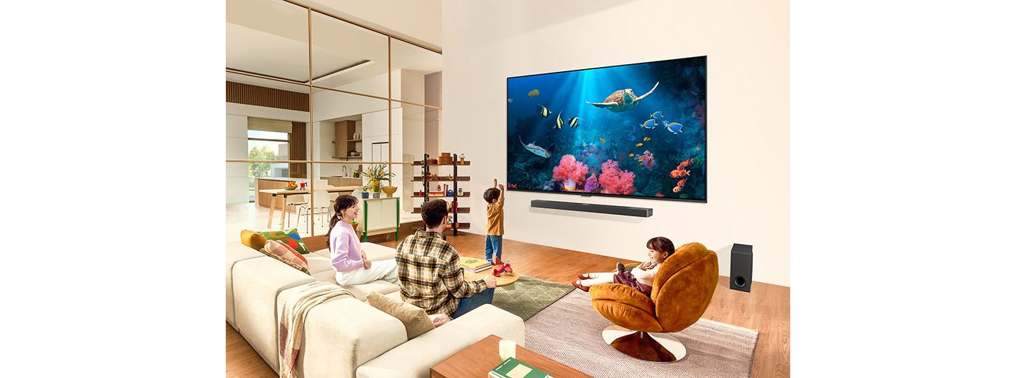 A family gathers around an ultra-large, wall-mounted LG QNED TV displaying an aquarium scene in their living room