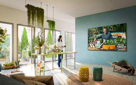 A woman watching a gardening lesson from the MasterClass app on her wall-mounted LG Smart TV as she tends to her plants