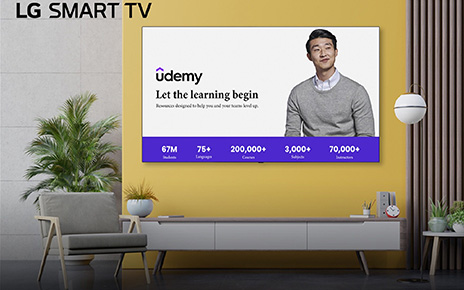A wall-mounted LG Smart TV displays Udemy’s home screen