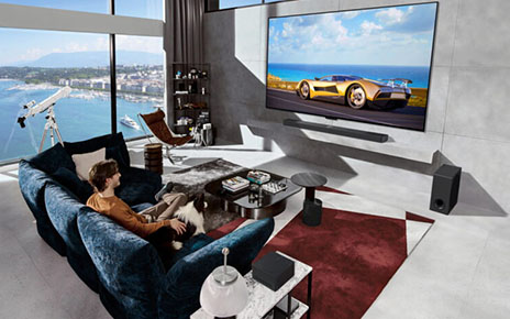A car displayed on a wall-mounted LG OLED evo M4 captures the attention of a man and his border collie