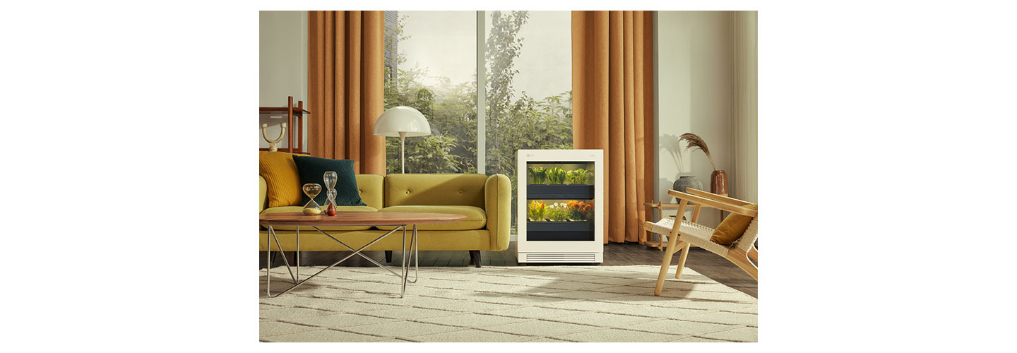 A front view of LG tiiun Nature Beige indoor gardening appliance next to a sofa in a living room.
