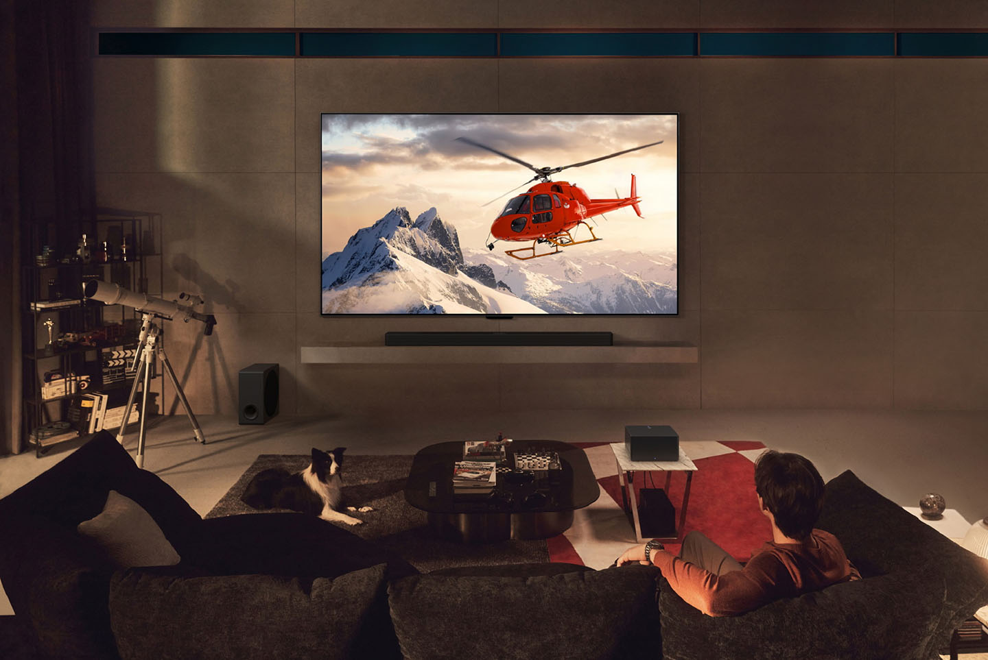 A man is watching a helicopter on the screen of a wall-mounted LG OLED M4, with a wireless Zero Connect Box sitting on a small table in the living space