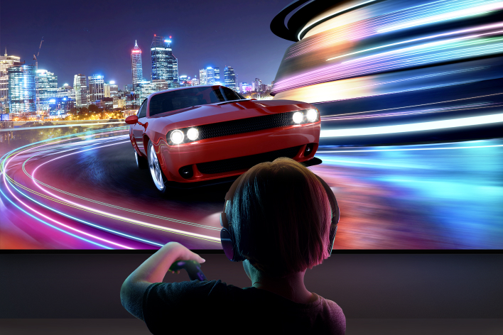 A young boy wearing headphones is seen from behind playing a car racing game on a large LG TV.