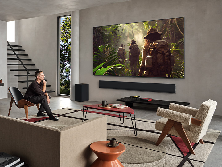 Wide view of a living room inside a premium home, a couple is watching a movie on their wall-mounted LG OLED TV. The TV's design blends elegantly with the wall and the interior design.