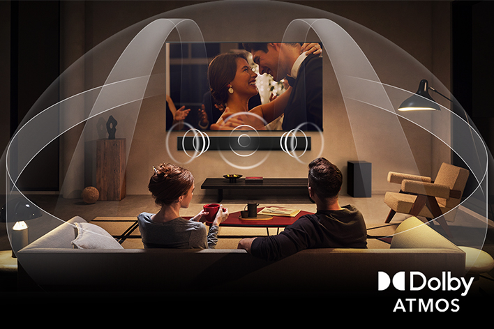 Dimly lit, cozy living room with an OLED LG TV with LG Soundbar. On the screen is a close-up of an electric guitar being played. Graphics show how Dolby Atmos fills the whole space with surround sound from all directions. Dolby Atmos logo is at the bottom corner.