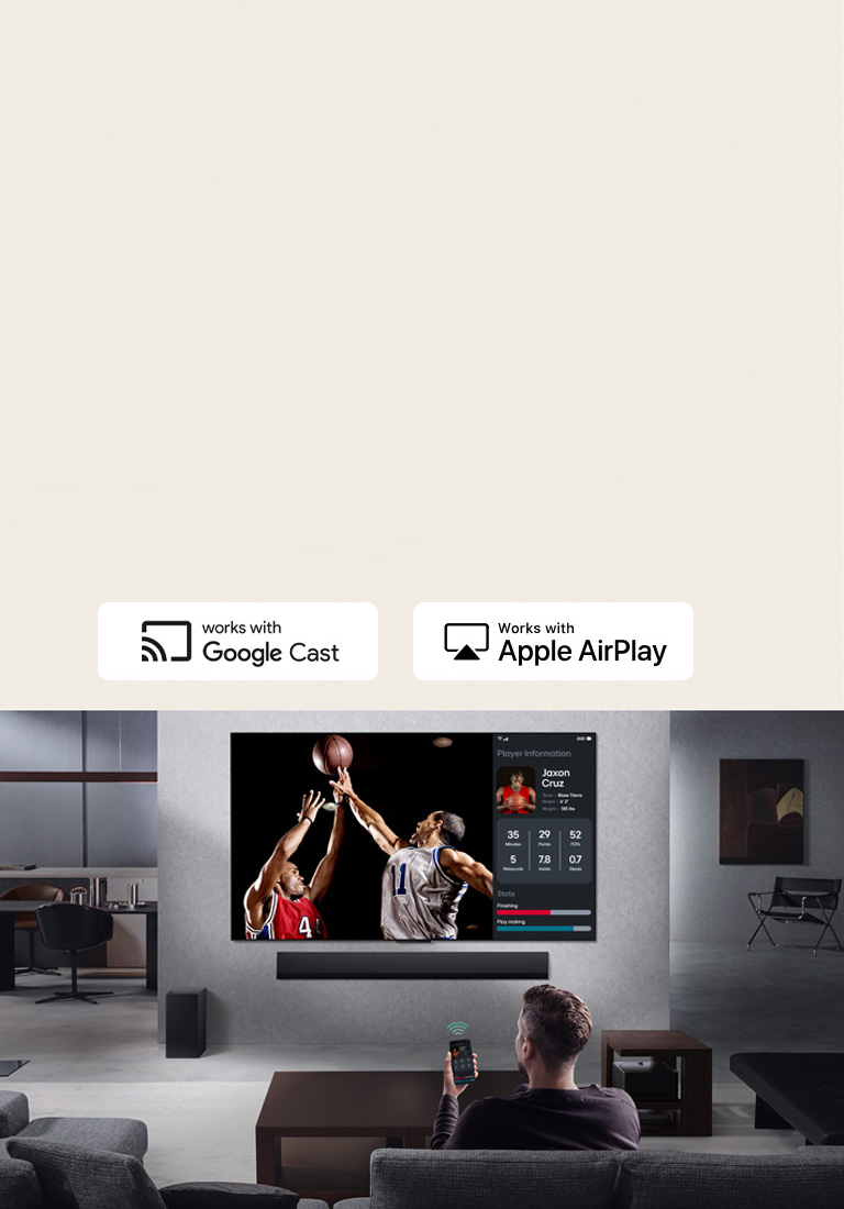 Person in their living room holding their phone. On the phone is a transmitting icon showing that the phone screen is being mirrored on the TV. On the TV is a basketball game to the side is the mirrored screen, showing player statistics. 