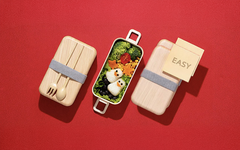 An image showing an easy bento box meal with penguin-shaped rice balls and colorful vegetables on a red background, illustrating a simple meal-prep concept.