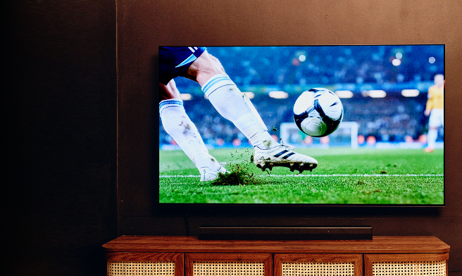 Large TV showing a soccer match above a wooden TV stand in a cozy living room.