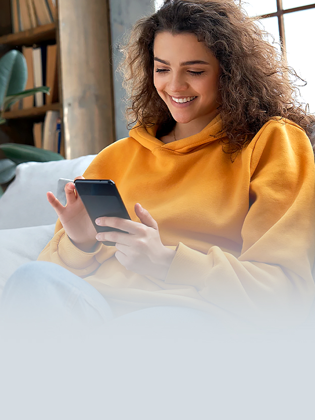 Woman smiling at her phone on a sofa illustrates Smart Diagnosis support for checking LG laundry product status through an app.