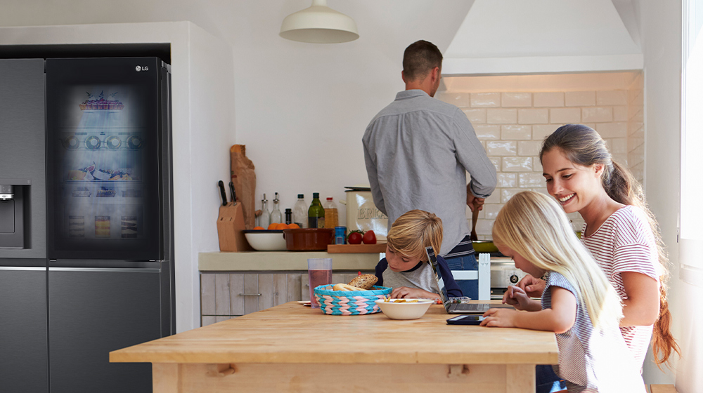 Modern kitchen with a large LG refrigerator on the left, a person cooking at the counter, and children at the table.