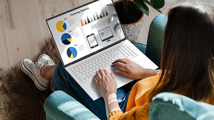 A person sitting comfortably in a chair, using a laptop that displays a presentation with charts and graphs. An animation demonstrates the anti-glare screen by showing no light reflection even when sunlight shines directly onto the display.