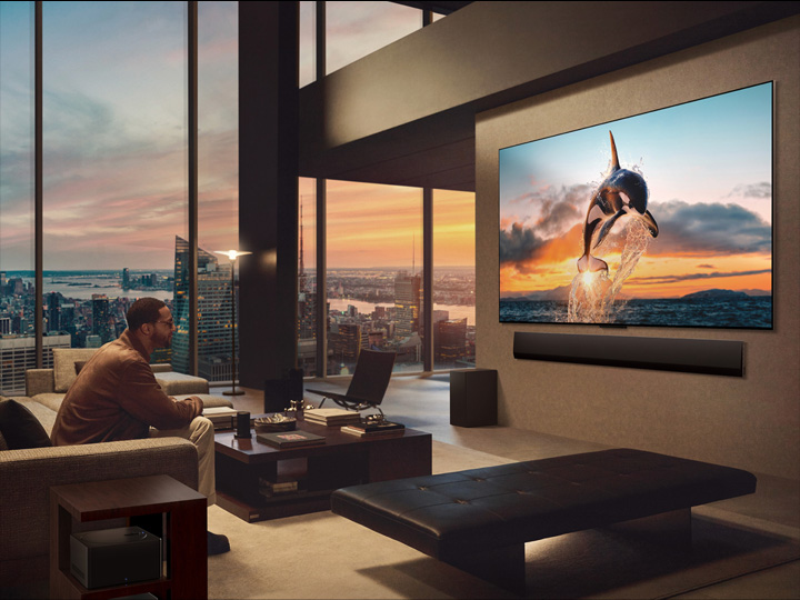 Spacious living room with a view of a cityscape. LG OLED TV is mounted on the wall with an LG Soundbar. The TV's One Wall Design allows it to be flush-fit against the wall and blend well with the space. Zero Connect Box is visible, but concealed.