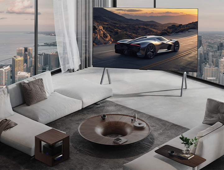 Spacious living room with a view of a cityscape. LG OLED TV is on a stand. The Ultra Slim Design makes the screen feel immersive. Zero Connect Box is visible, but concealed.