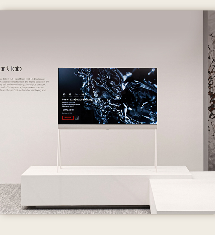 Una imagen de un televisor Easel en una habitación blanca que muestra en pantalla una escultura negra hecha con arte digital. La habitación se refleja en una escultura plateada ubicada a la derecha del televisor.