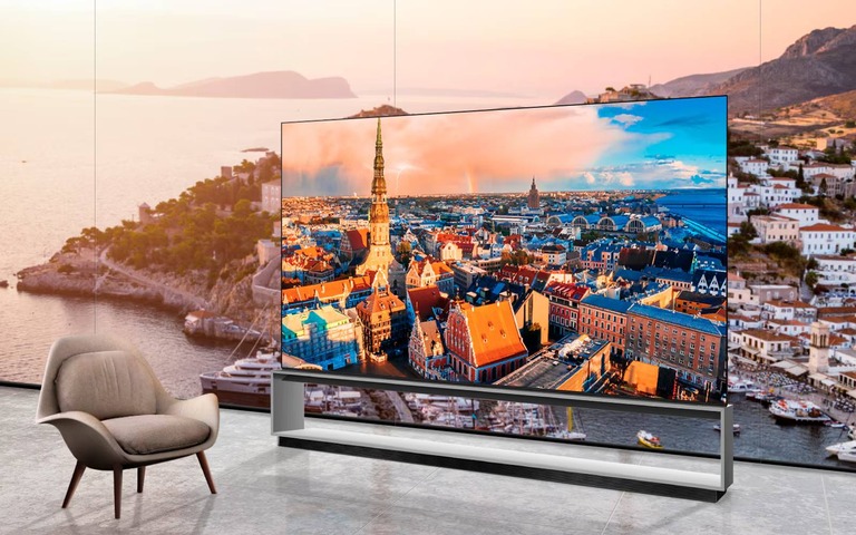 A modern living space featuring an LG TV displaying a vibrant cityscape with colourful rooftops and a tall spire, positioned next to a stylish armchair and overlooking a scenic coastal backdrop