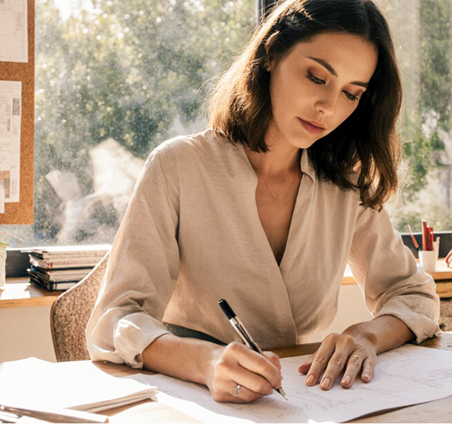 A woman dressed in white sits next to a desk with interior information spread out on it.